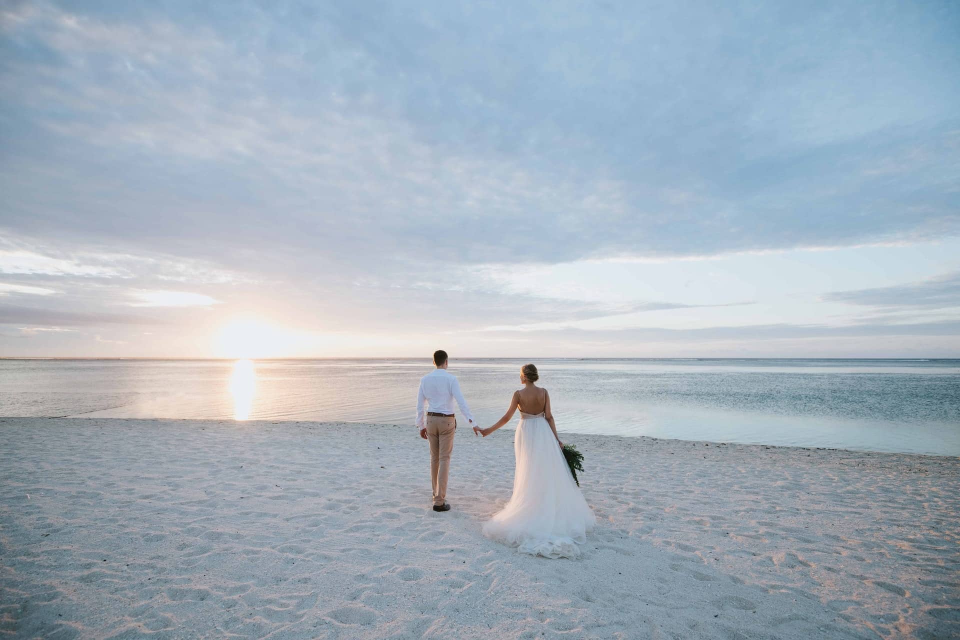Mauritius. Et brudepar som går på en hvit sandstrand i solnedgang