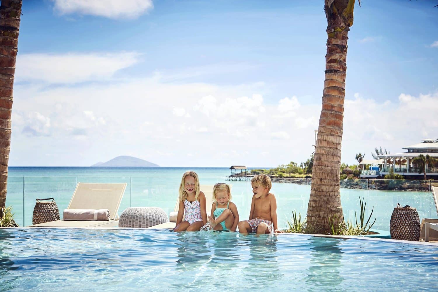 Tre barn som koster seg ved bassengkanten med blått hav i bakgrunnen på Mauritius