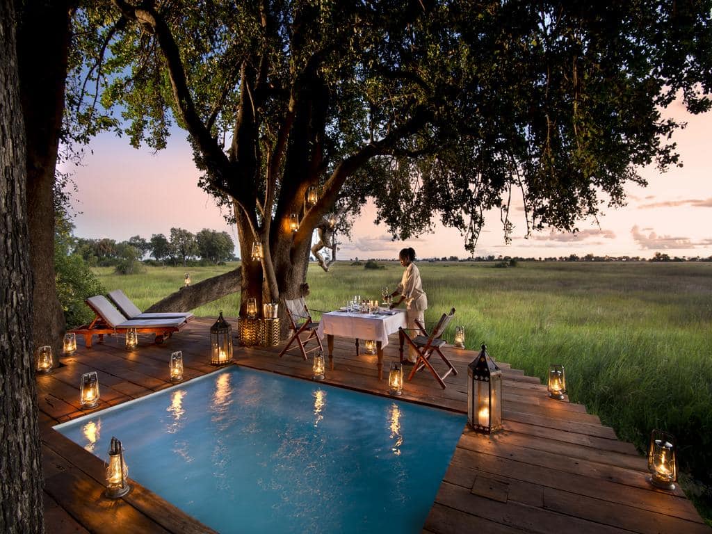 Duba Plains Camp Botswana. Utendørsbasseng med lys og bord for to.